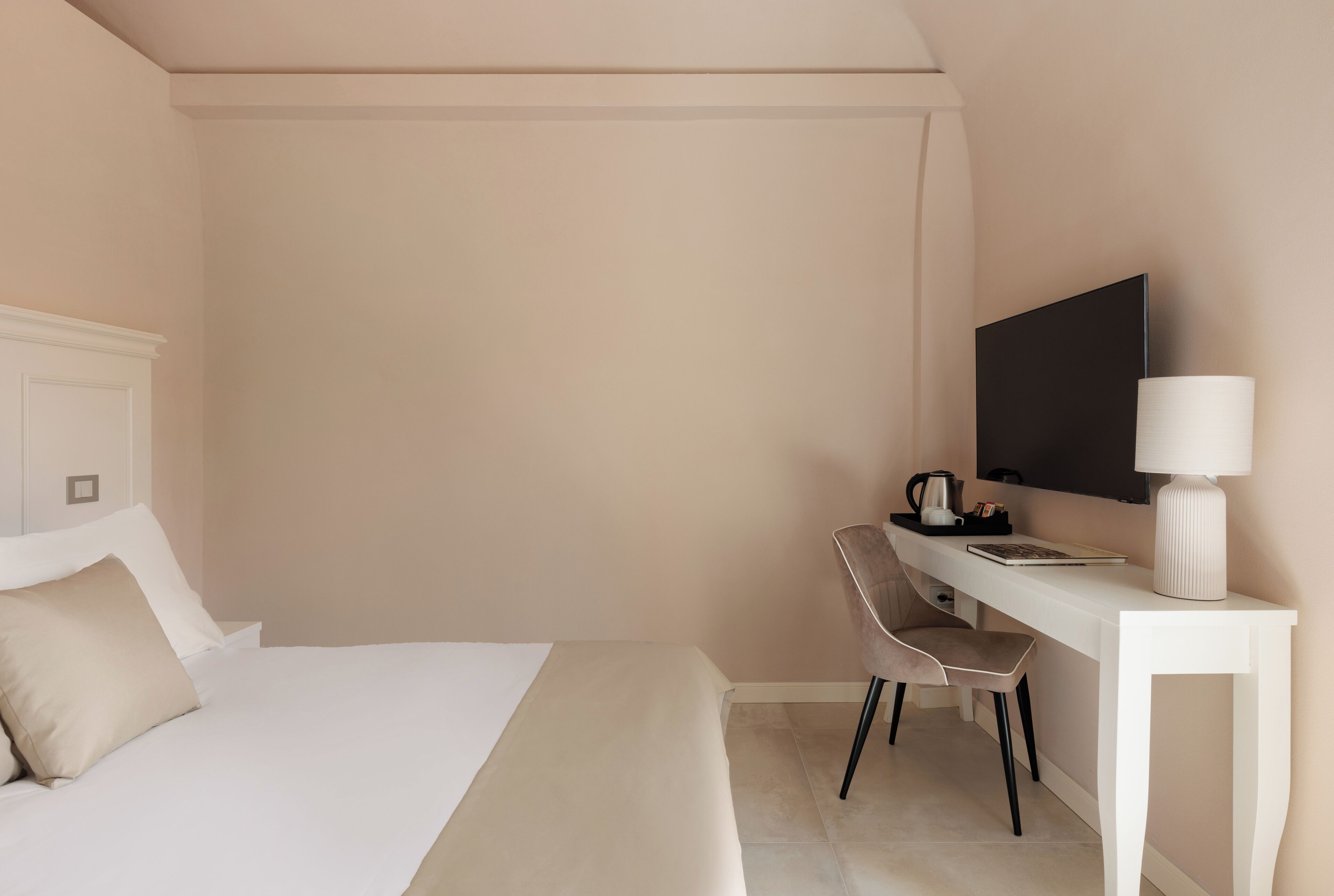 Habitación de hotel con cama, escritorio, silla, televisor de pantalla plana y lámpara.