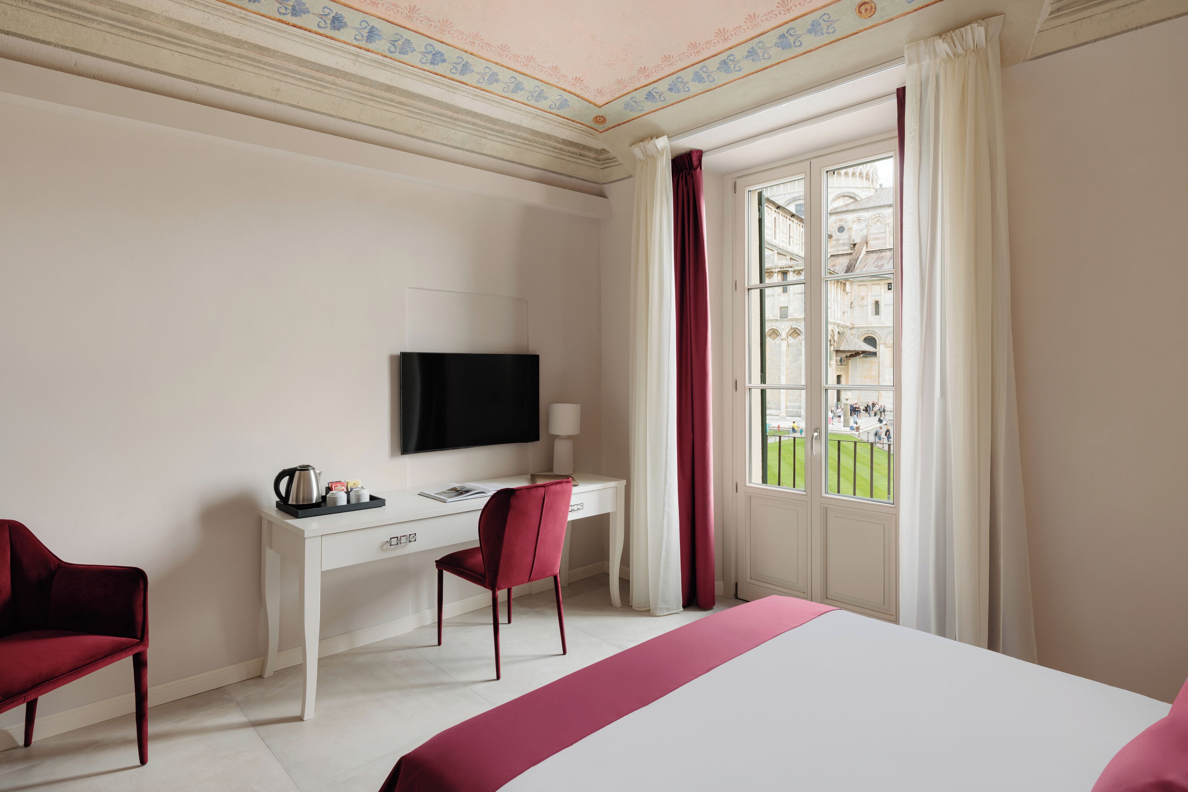 Habitación de hotel con cama, escritorio con televisor, silla y ventana con cortinas.