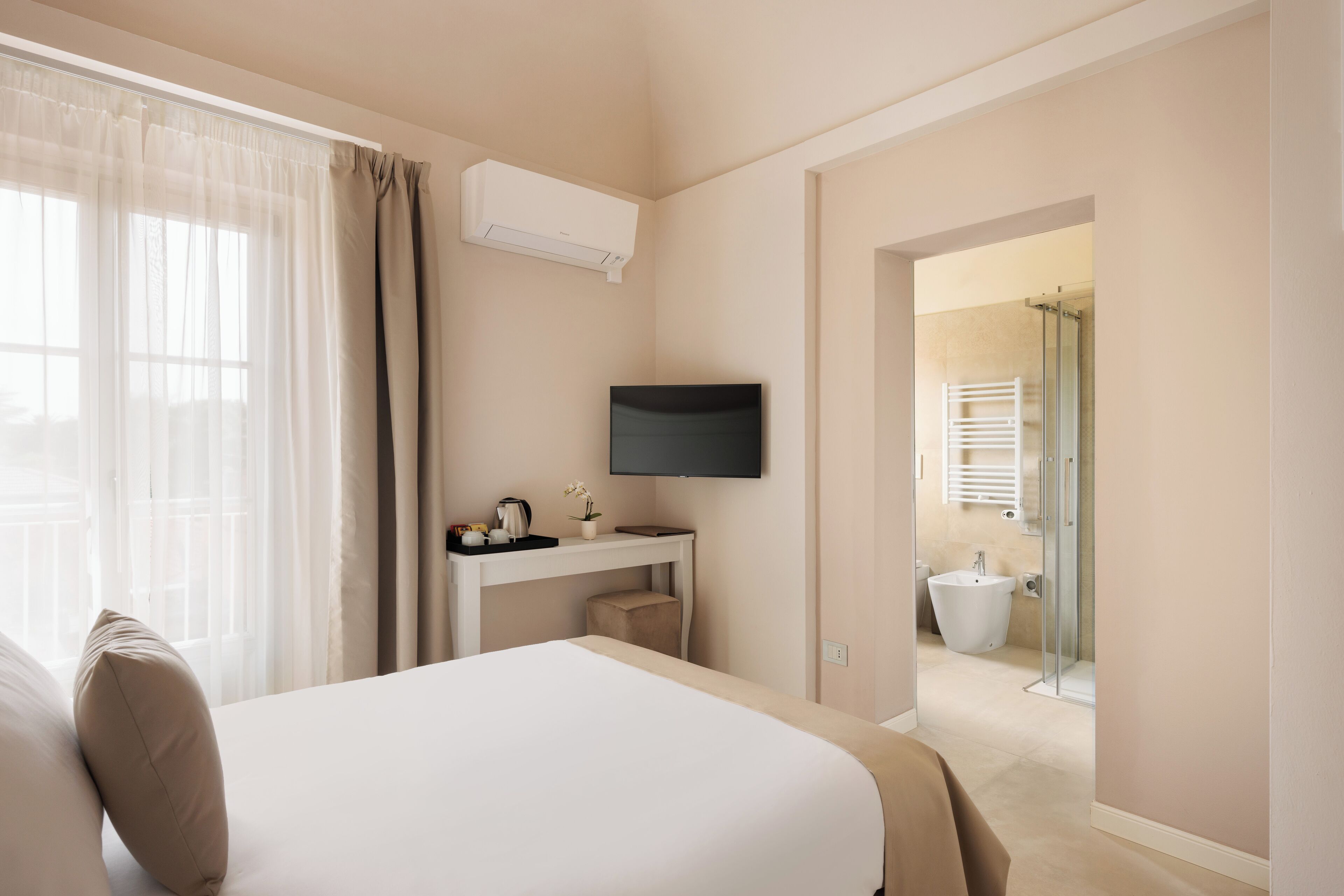 Ein Hotelzimmer mit Bett, Schreibtisch, Flachbildfernseher, einem Fenster mit Vorhängen und einem sichtbaren Badezimmer durch eine offene Tür.