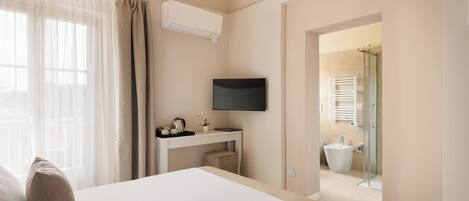 Ein Hotelzimmer mit Bett, Schreibtisch, Flachbildfernseher, einem Fenster mit Vorhängen und einem sichtbaren Badezimmer durch eine offene Tür.