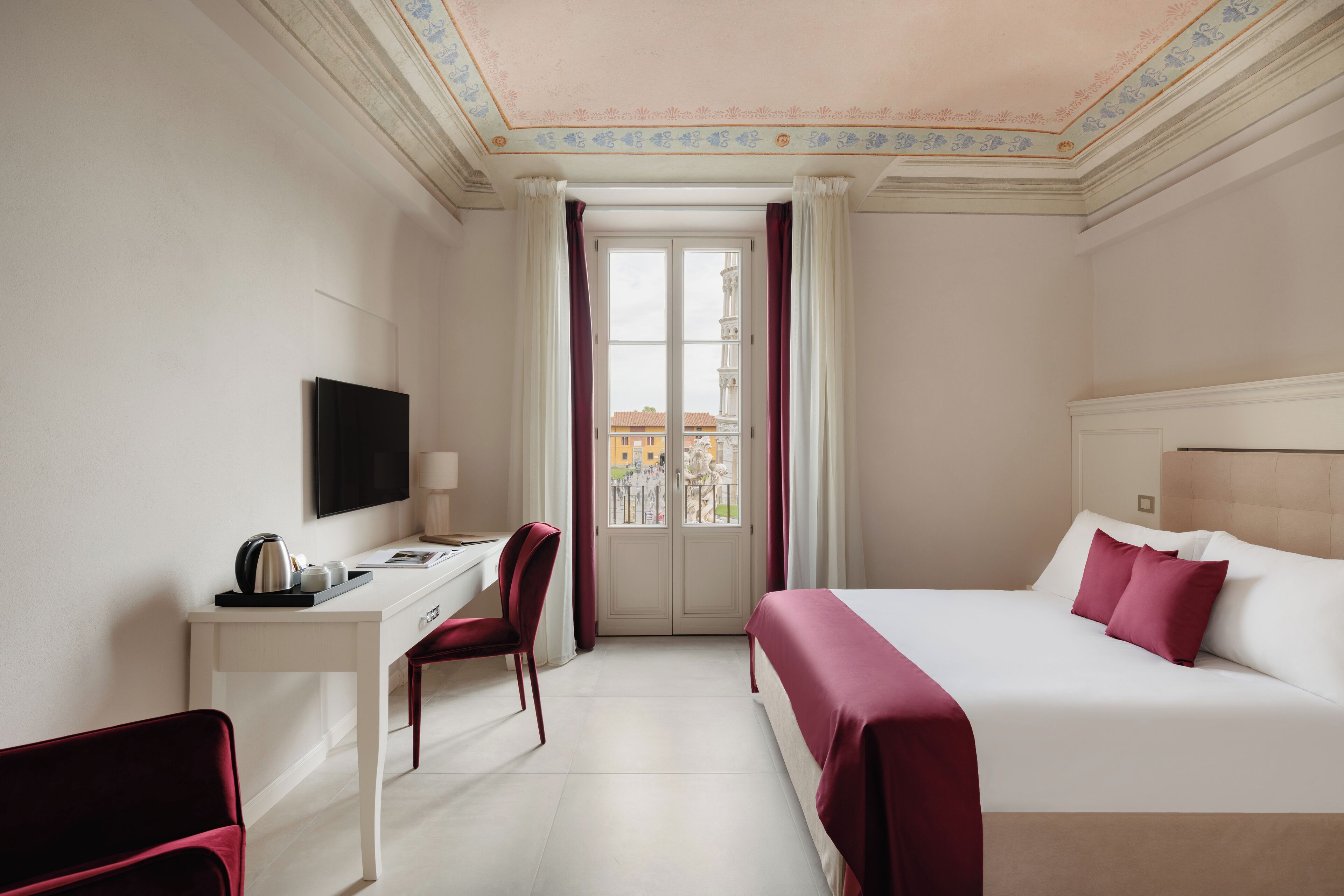 A hotel room with a bed, a desk, a chair, a TV, and a view of the city through a window.