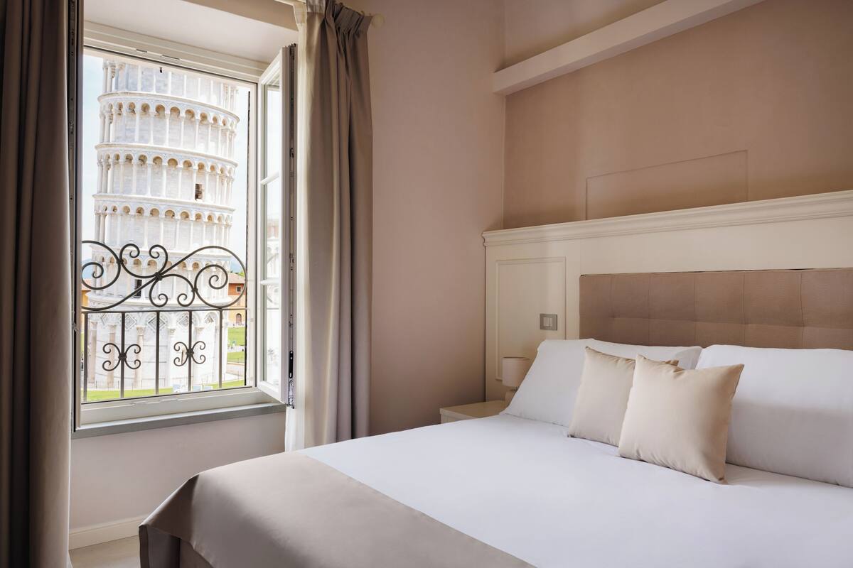 A hotel room with a bed, a nightstand, a window with a view of a famous tower, and a curtain.