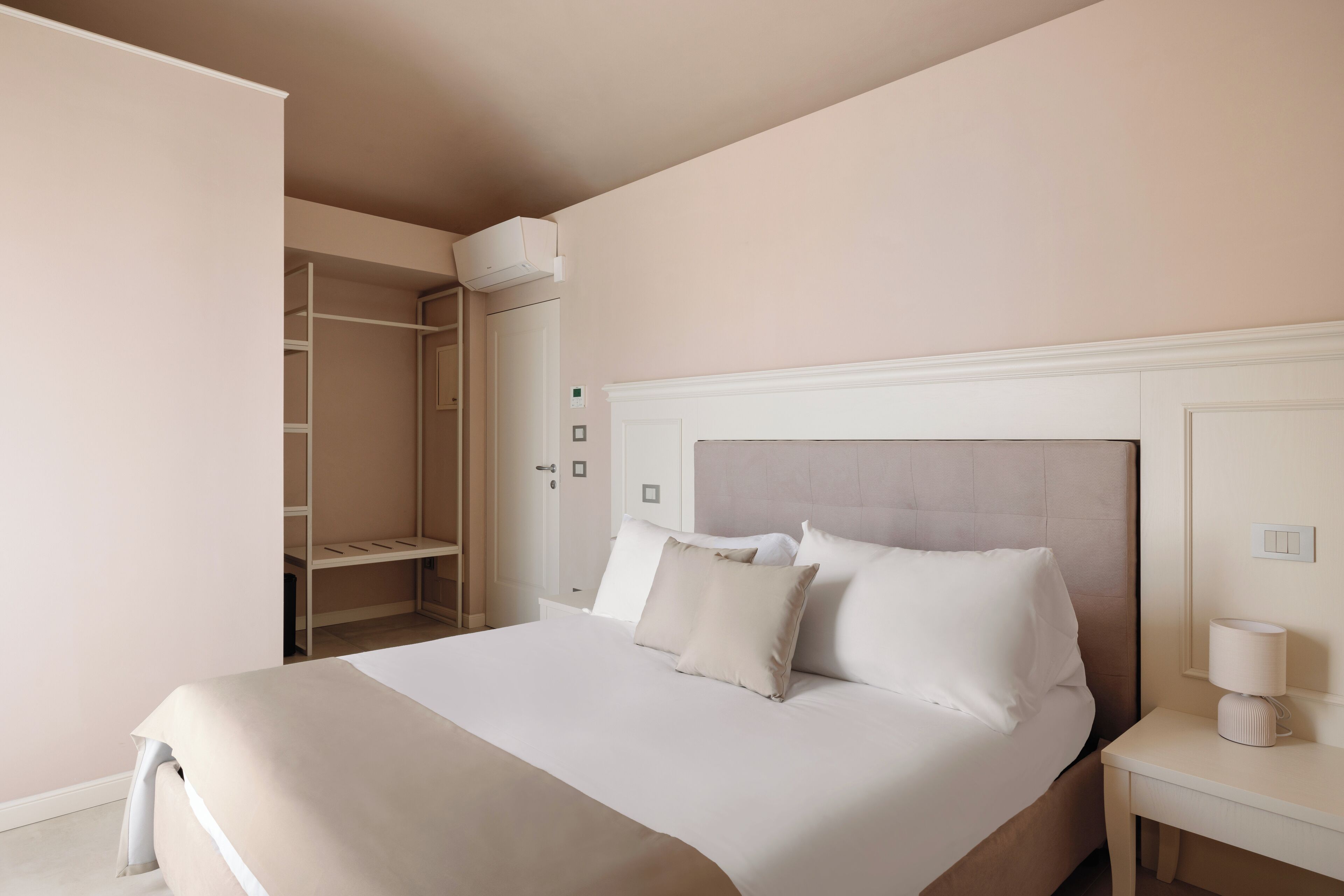 A neatly arranged hotel room with a large bed, a bedside table with a lamp, and a wardrobe with a hanging organizer.