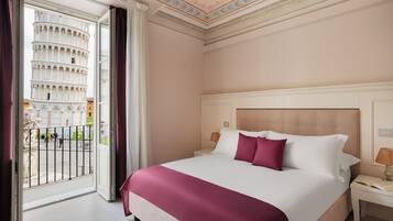 Habitación de hotel con una cama grande, una mesita de noche, una ventana con vistas a la Torre Inclinada de Pisa y un balcón con barandilla.