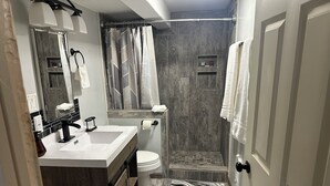 Een badkamer met een houten wastafelmeubel, een witte wastafel, een toilet en een douchecabine met gordijn.