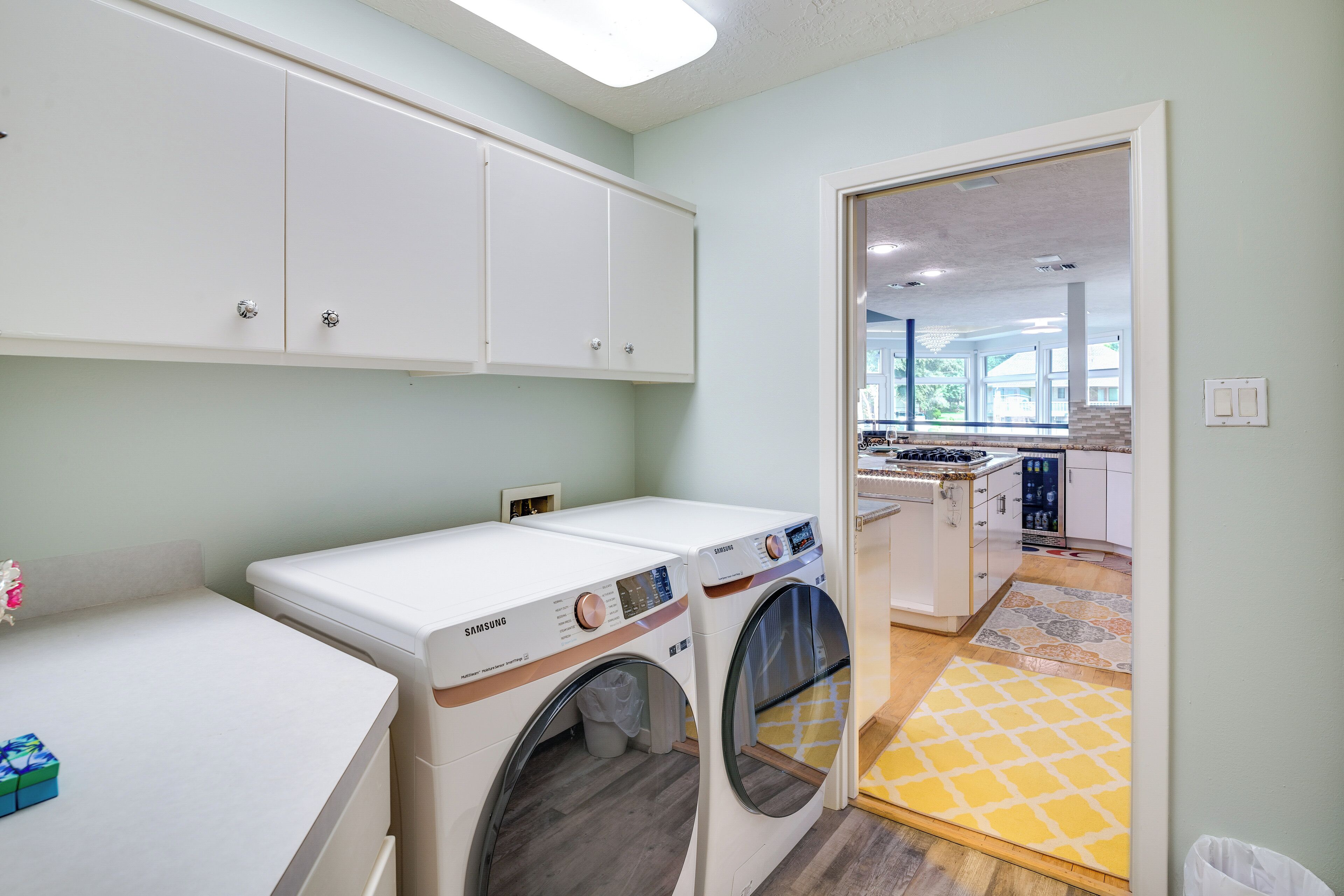 A laundry room with two Samsung washing machines, a white countertop, and a yellow patterned rug.