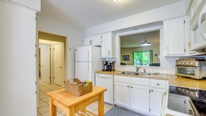 A kitchen with white cabinets, a wooden table, a basket, a dishwasher, a stove, and a window with a view of greenery. - Bella Vista Townhome w/ Deck Near Back 40 Trail! (Bella Vista)
