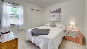A bedroom with a bed, a nightstand with a lamp, a window with curtains, and a painting on the wall. - Bella Vista Townhome w/ Deck Near Back 40 Trail! (Bella Vista)