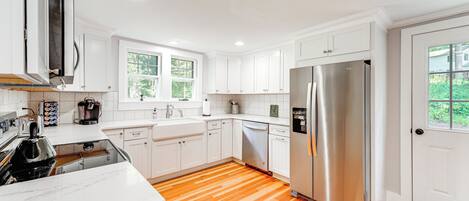 A modern kitchen with white cabinets, stainless steel appliances, and wooden flooring.