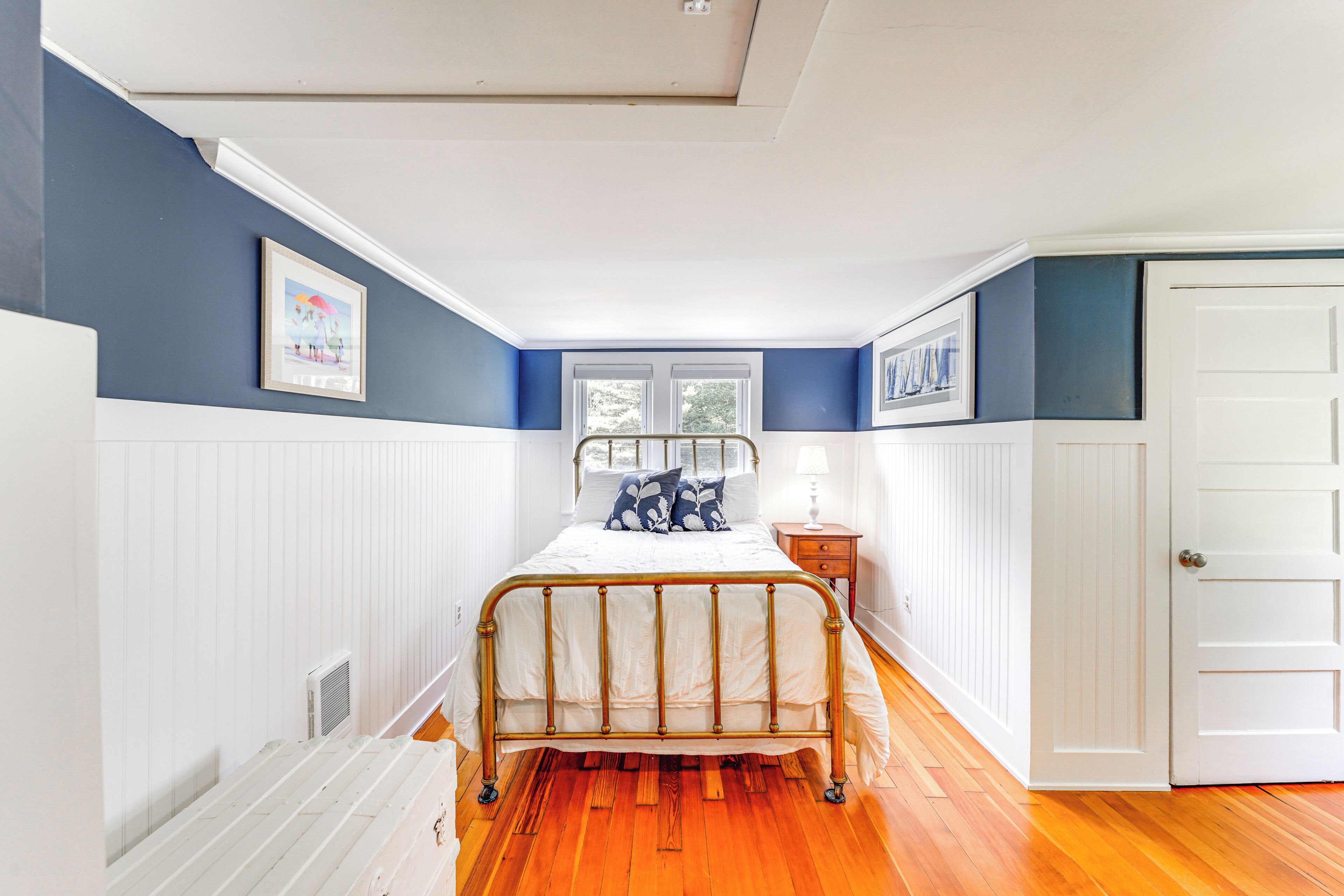Un dormitorio con cama de madera, paredes blancas, detalles en azul, una ventana y una puerta.