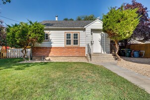 A single-story house with a brick foundation and white siding, a front yard with a lawn and two trees, and a wooden fence in the background.