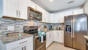 A modern kitchen with white cabinets, stainless steel appliances, a tiled backsplash, and granite countertops. - 5 Mi to Disney World: Spacious Kissimmee Home! (Kissimmee)