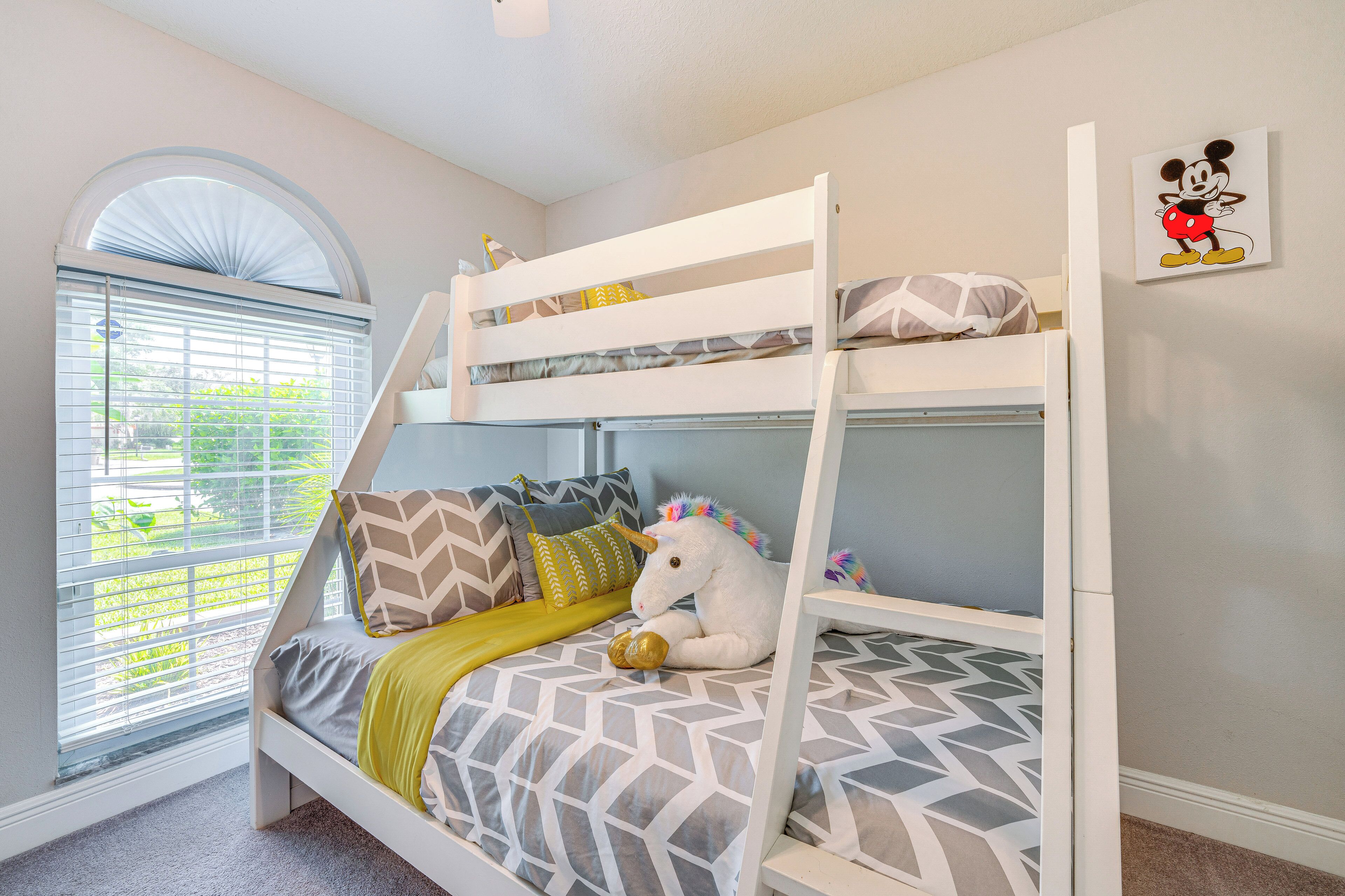 A bunk bed with a unicorn plush toy, patterned bedding, and a Mickey Mouse wall art.