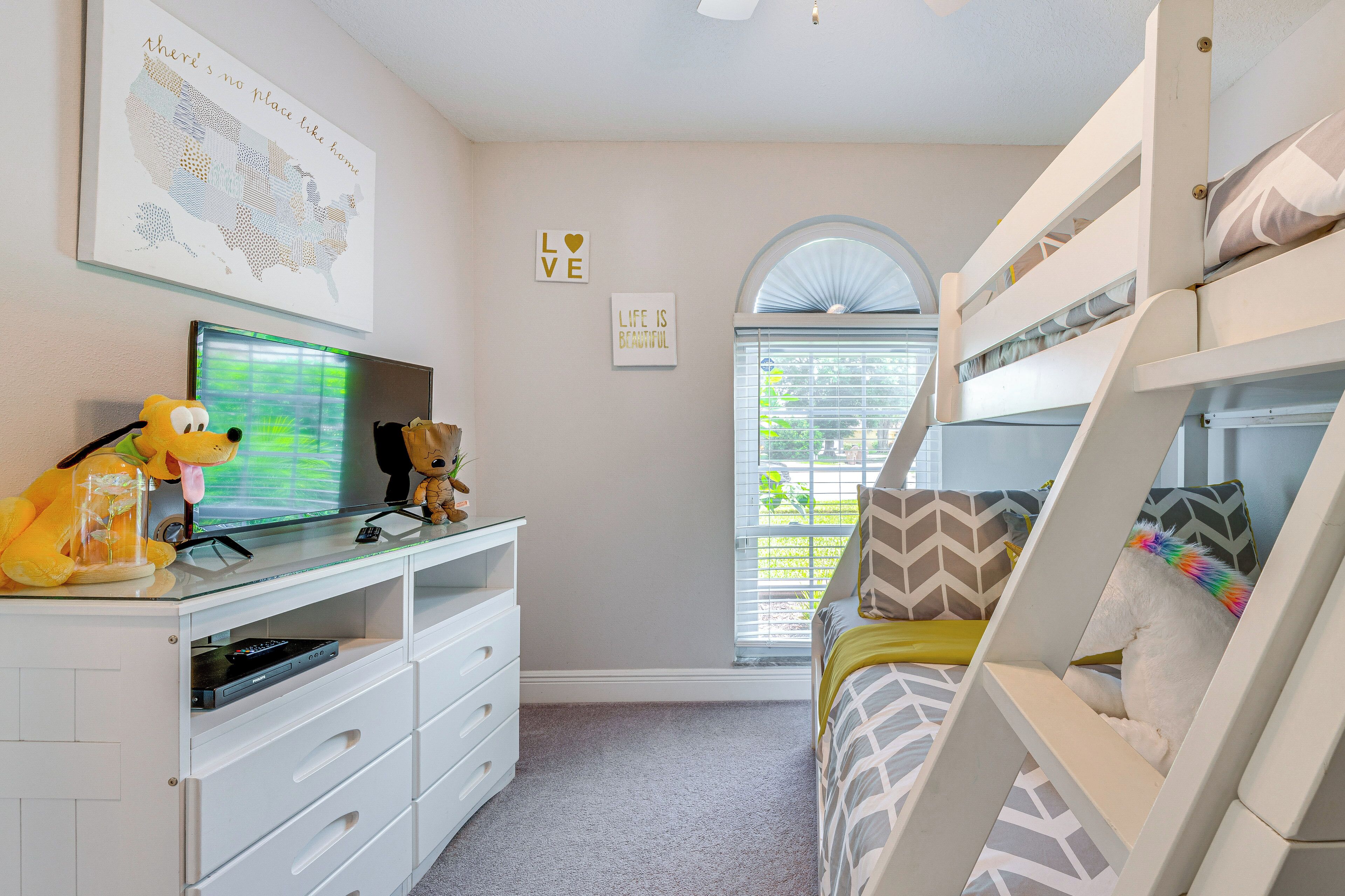 A child's bedroom with bunk beds, a TV, a desk, and a window with blinds.