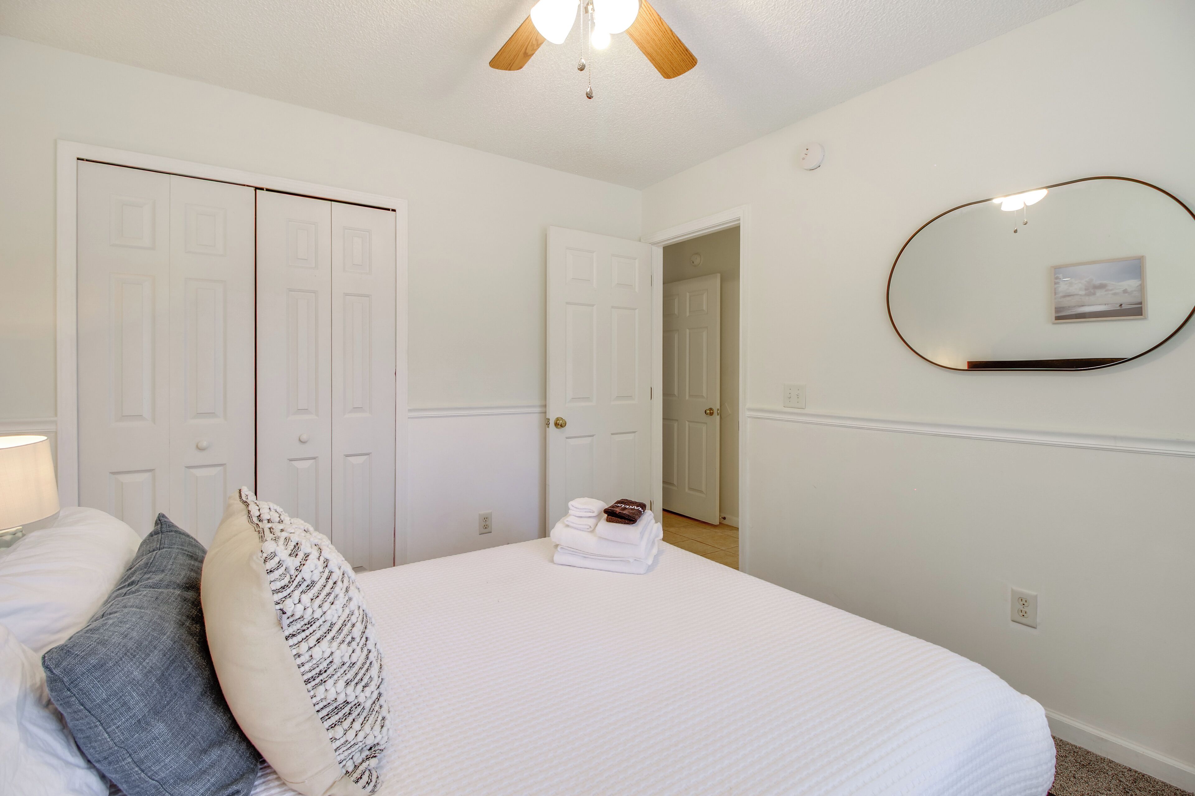 Une chambre à coucher avec un lit, une table de chevet, une lampe, un ventilateur de plafond et une porte.