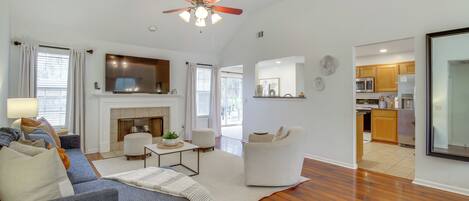 A spacious living room with a fireplace, a ceiling fan, and a kitchen area visible through an open doorway.