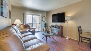 A living room with a leather sofa, a glass coffee table, a TV mounted on the wall, and a floor lamp.