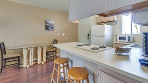 A compact kitchen with a white refrigerator, a microwave, and a sink. There is a wooden dining table with two stools and a small island with a sink.