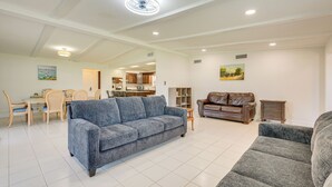 Ein großzügiger Wohnraum mit einem blauen Sofa, einem braunen Ledersofa und einem grauen Sofa. Ein Essbereich mit einem Holztisch und Stühlen ist ebenfalls vorhanden. Im Hintergrund ist eine Küche zu sehen.