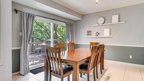 A dining area with a wooden table and chairs, a large window with curtains, and a view of the outdoors. - Deck & Greenbelt Access: Lovely Austin Home (Austin)