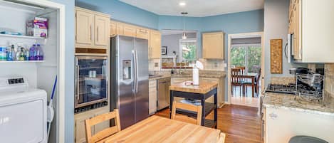 A modern kitchen with wooden cabinets, a stainless steel refrigerator, a built-in oven, and a dining area with a wooden table and chairs.