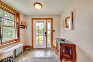 Un pasillo con piso de piedra, un banco de madera, un radiador, una puerta con paneles de vidrio y una pequeña mesa de madera.