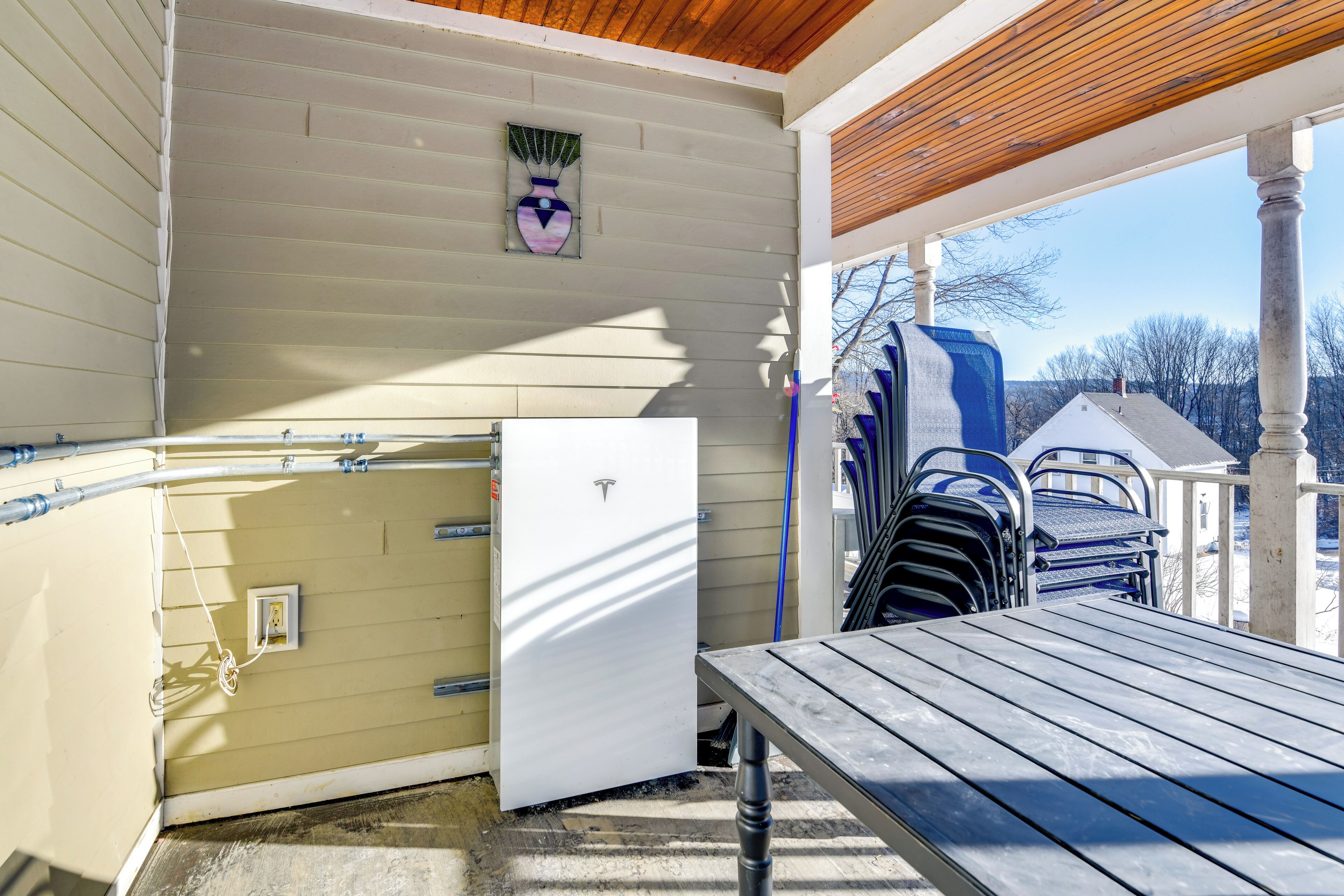 A covered outdoor area with a table and chairs, a white refrigerator, and a blue mailbox.