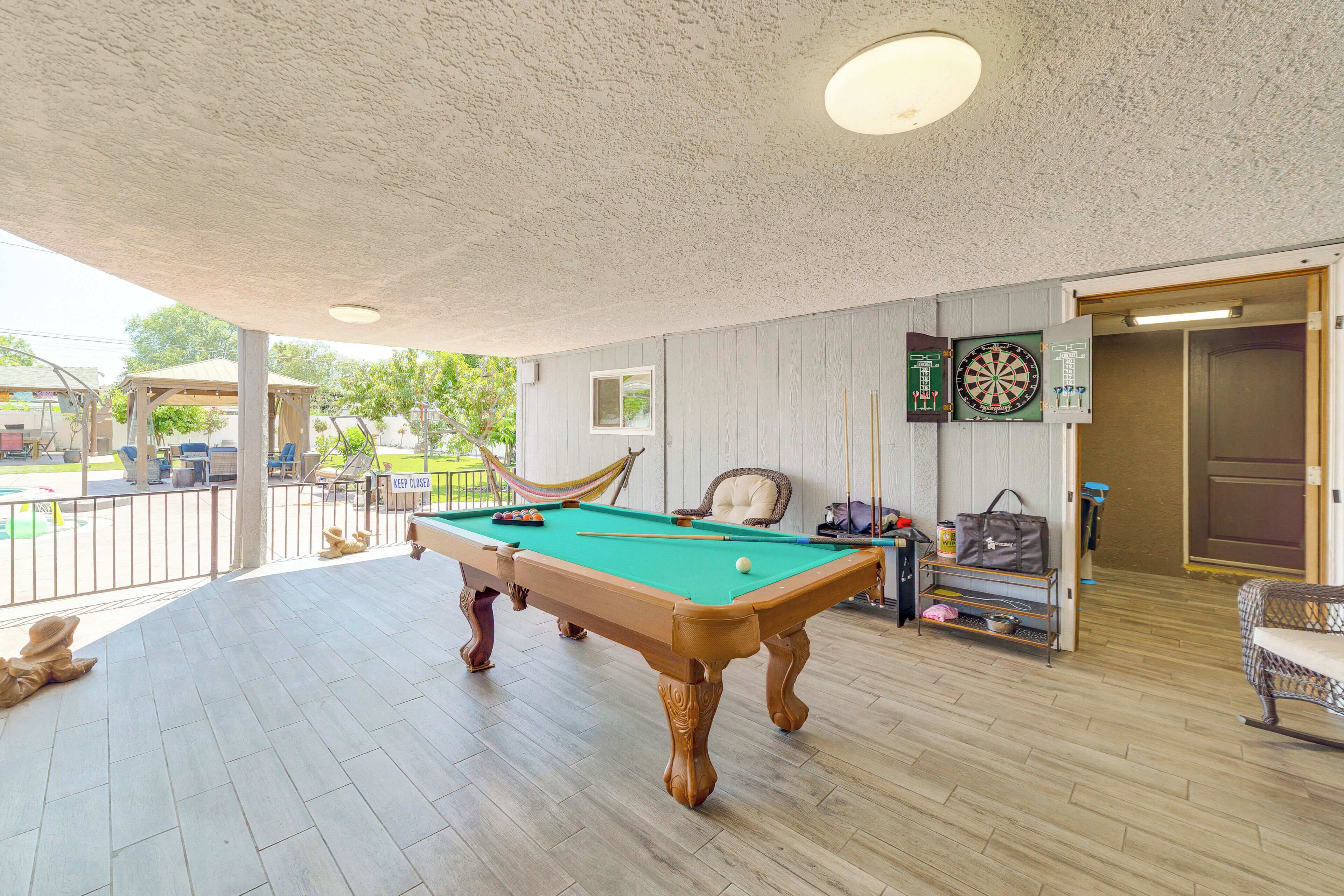 Une table de billard dans une pièce donnant sur une piscine, un jeu de fléchettes et une porte menant à une autre pièce.