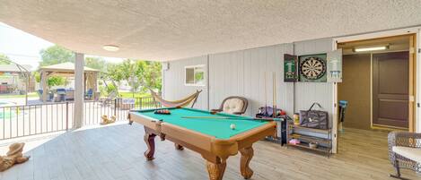 Une table de billard dans une pièce donnant sur une piscine, un jeu de fléchettes et une porte menant à une autre pièce.