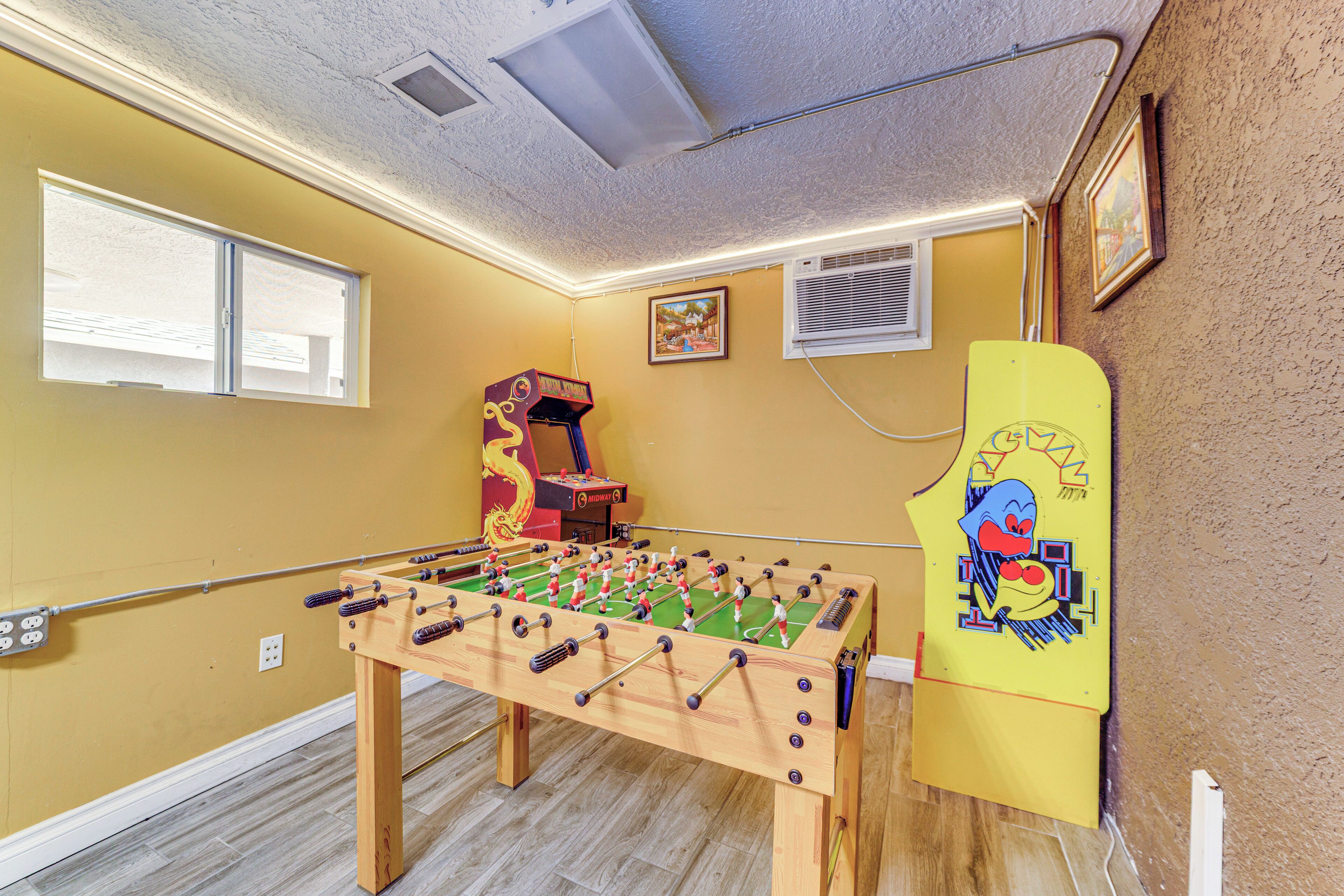 A room with a foosball table, a small arcade machine, and a yellow paddle sports table.