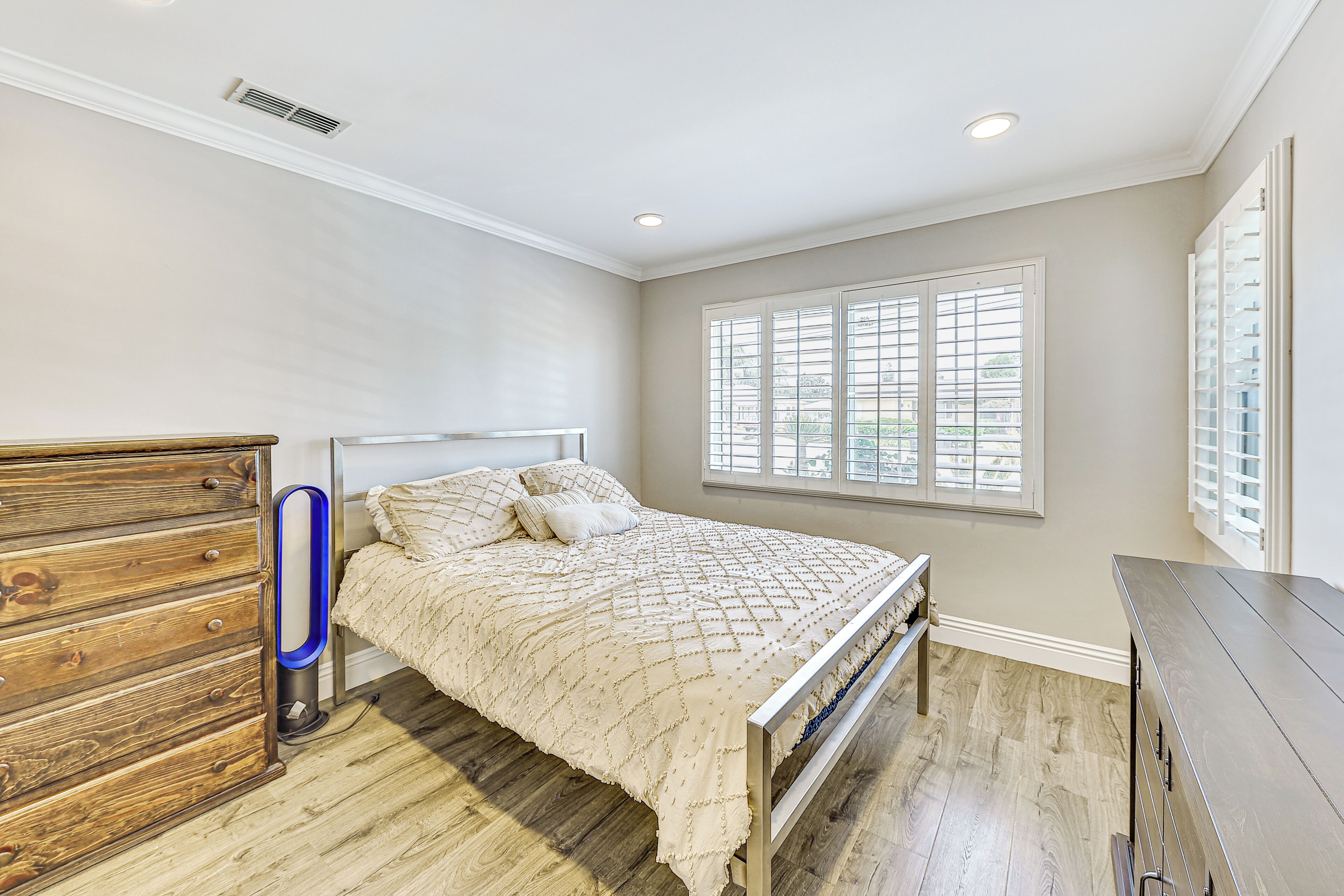 A bedroom with a bed, wooden dresser, and a window with blinds.