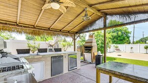 Un espacio cocina al aire libre con una parrilla, un refrigerador y una mesa.