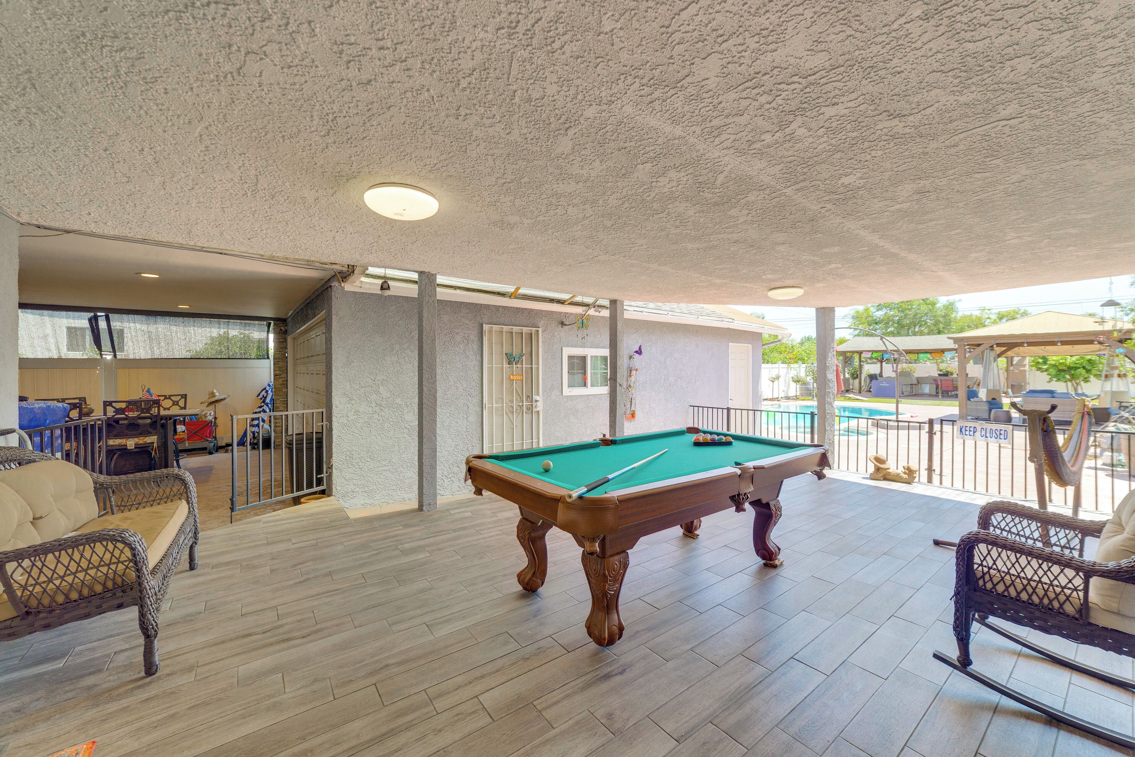 An indoor pool area with a pool table, wicker furniture, and a view of a pool outside.