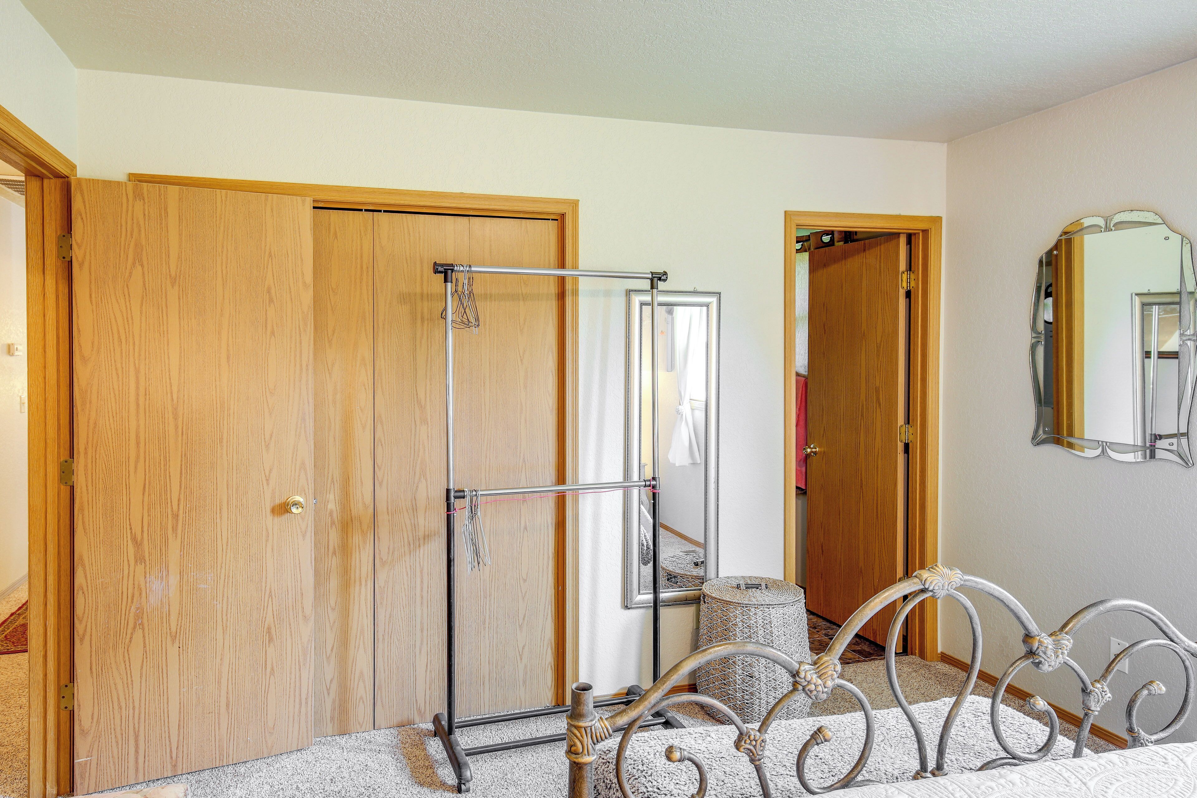 A bedroom with a wooden wardrobe, a metal bed frame, a mirror, and a small round ottoman.