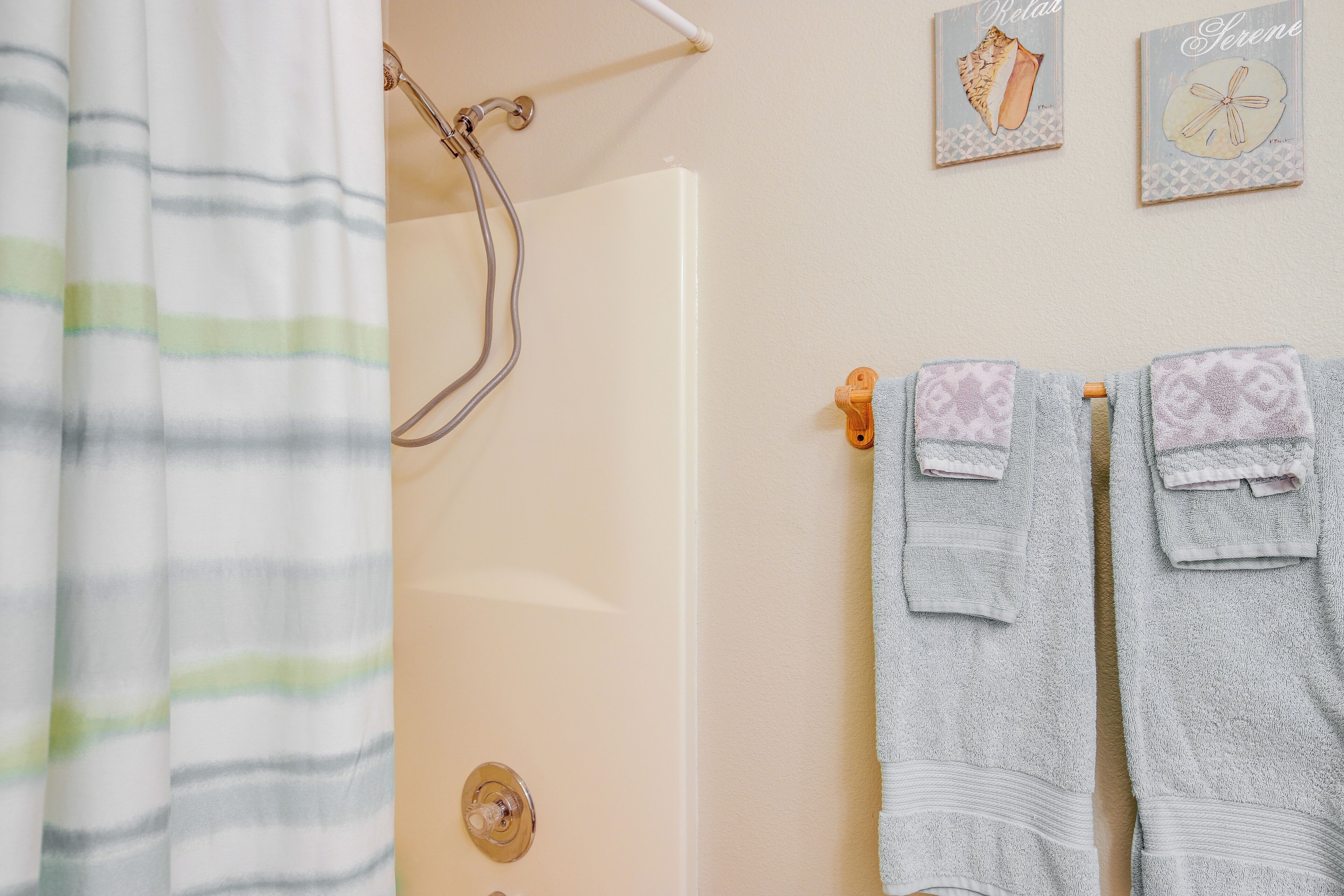 A bathroom with a shower curtain, a towel rack with two towels, and two framed pictures on the wall.