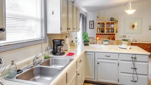 Una cucina con mobili bianchi, un lavello doppio, una macchina da caffè e una finestra con persiane.