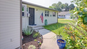 Una casa a un piano con portico anteriore, un piccolo giardino con diverse piante e una bandiera americana.