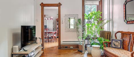A spacious living room with hardwood flooring, a wooden bench, a large potted plant, and a television on a stand.