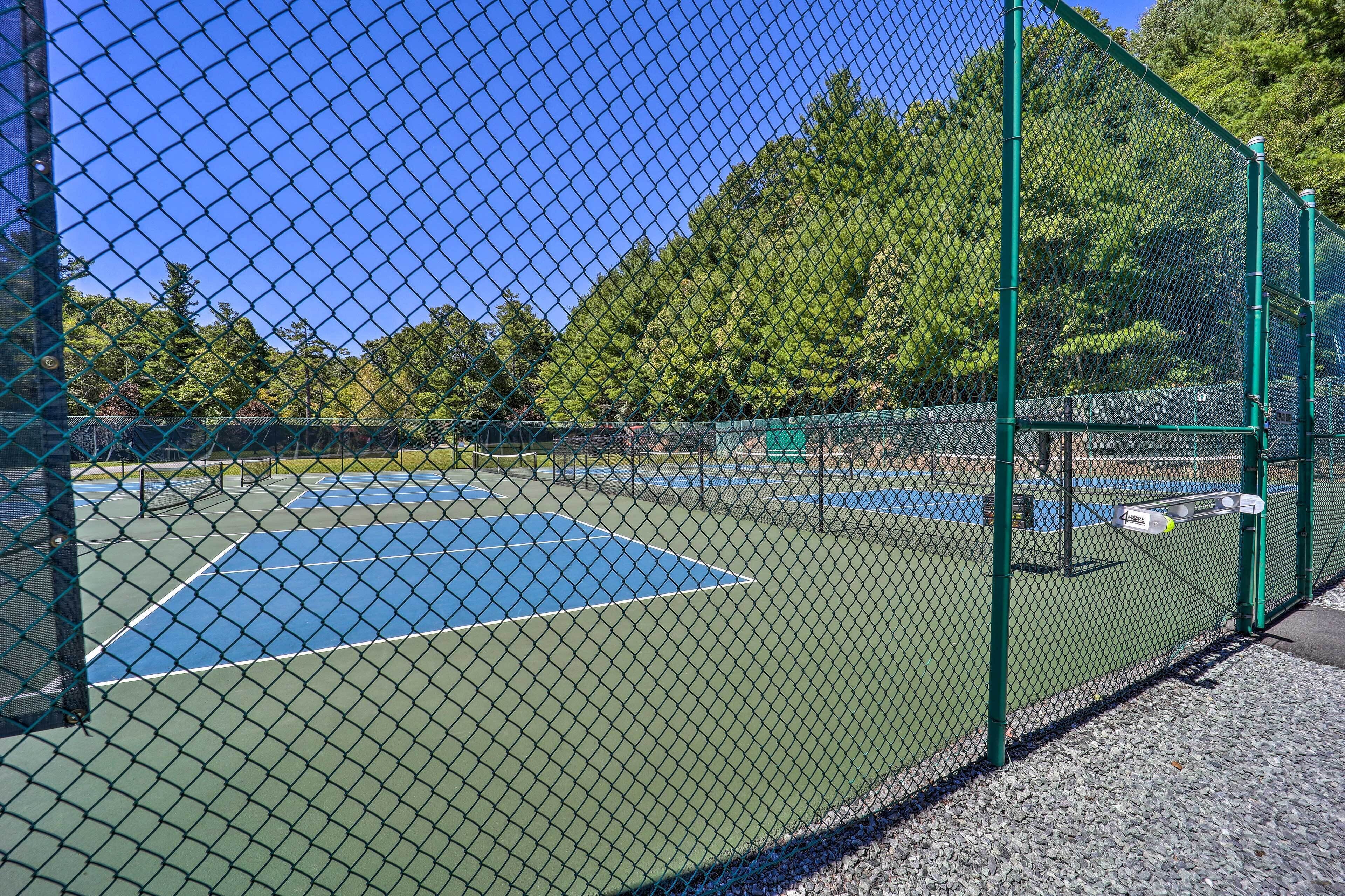 A tennis court enclosed by a green chain-link fence with trees in the background.