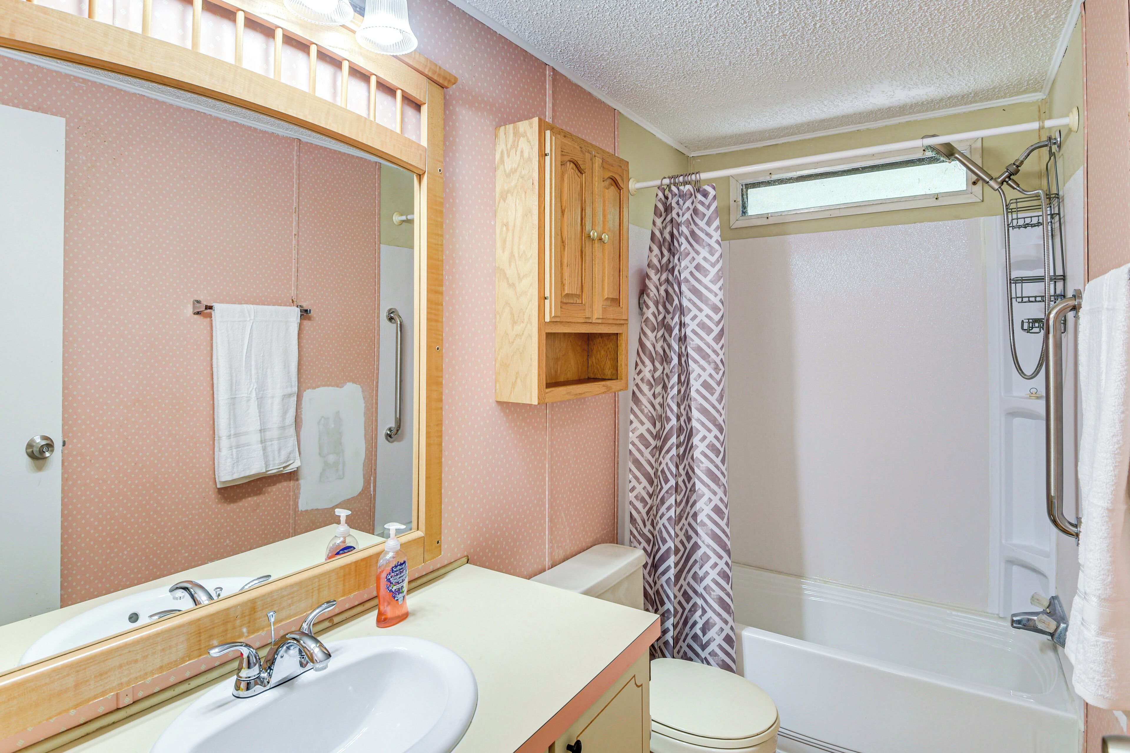 A bathroom with a sink, mirror, toilet, shower, and wooden cabinet.