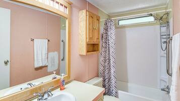 A bathroom with a sink, mirror, toilet, shower, and wooden cabinet.