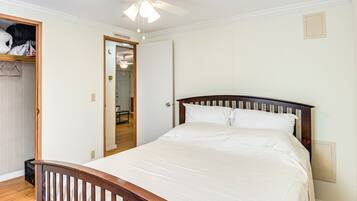 Une chambre à coucher avec un lit en bois, du linge de lit blanc, un ventilateur de plafond et un dressing.