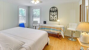 Un dormitorio con cama, escritorio, silla, ventilador de techo y ventana.
