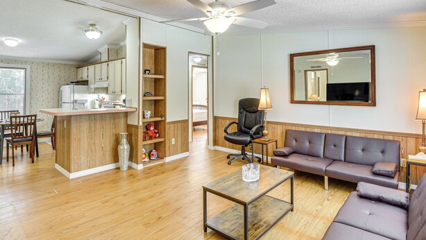Una sala de estar moderna con piso de madera, un sofá, una mesa de centro y una cocina con alacenas y un refrigerador.