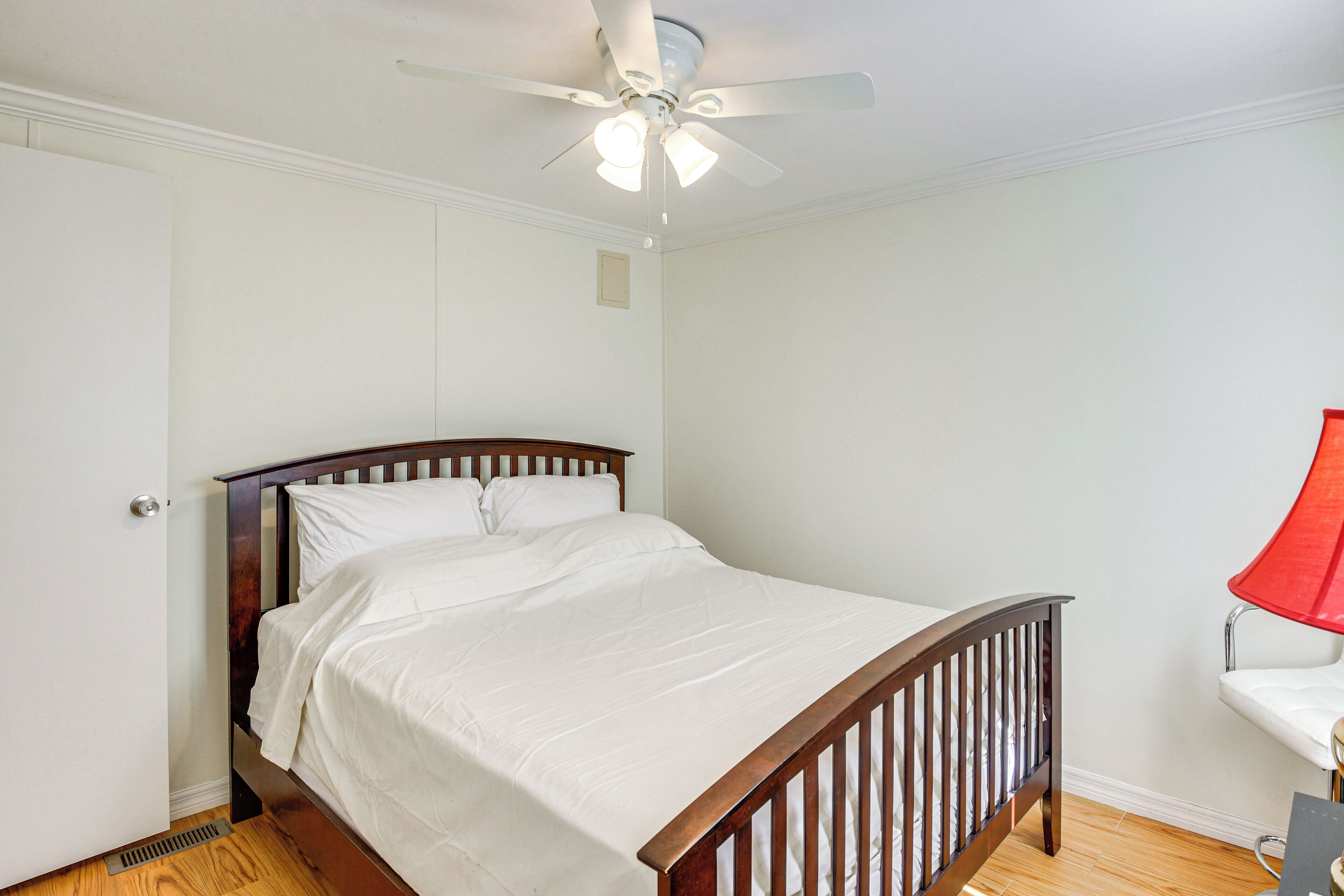 Une chambre à coucher avec un lit en bois, du linge de lit blanc, un ventilateur de plafond et une lampe rouge.