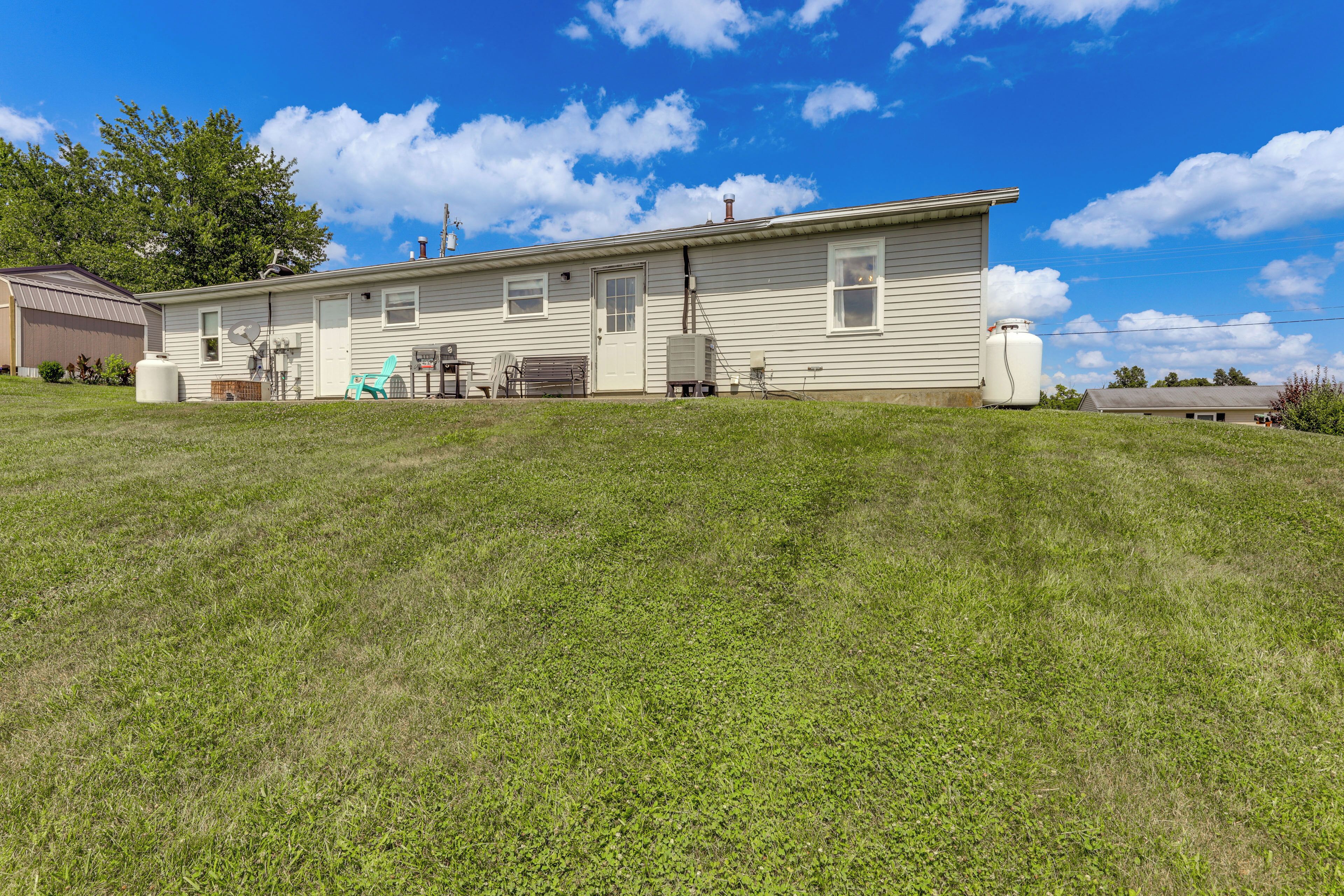 A single-story mobile home with a front porch, a satellite dish, and a large water tank in the backyard.