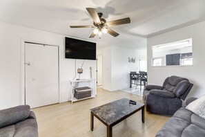 A modern living room with a ceiling fan, a flat-screen TV, a gray sofa, a coffee table, and a dining area with a table and chairs. - Quiet Dry Ridge Home w/ Yard - Near Ark Encounter! (Dry Ridge)