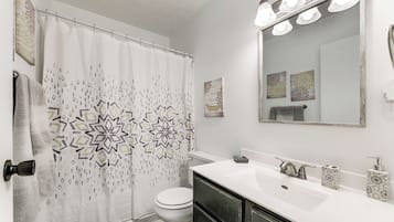 A bathroom with a shower curtain, toilet, sink, and mirror.