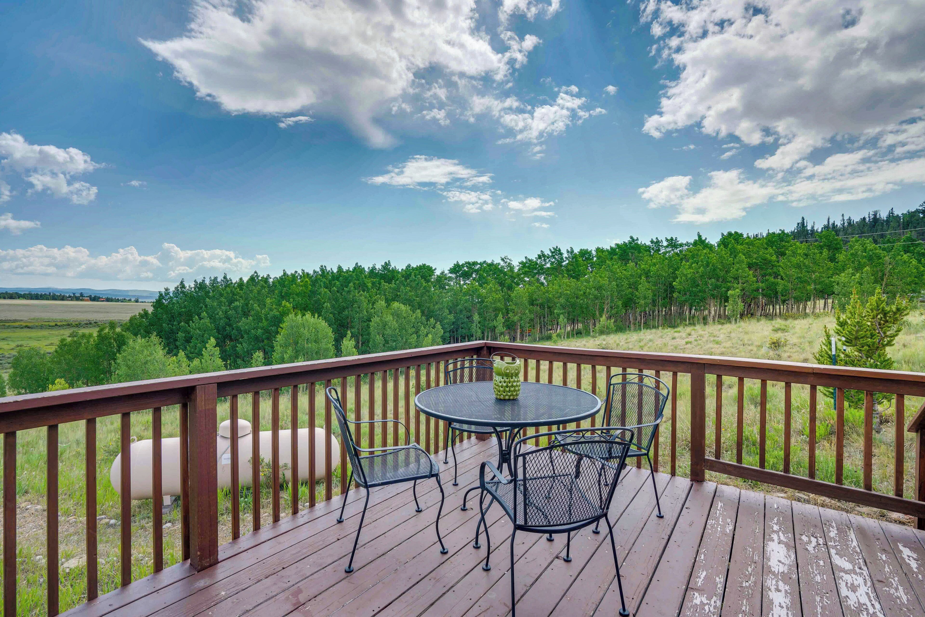 A wooden deck with a round table and four chairs, overlooking a forested landscape.