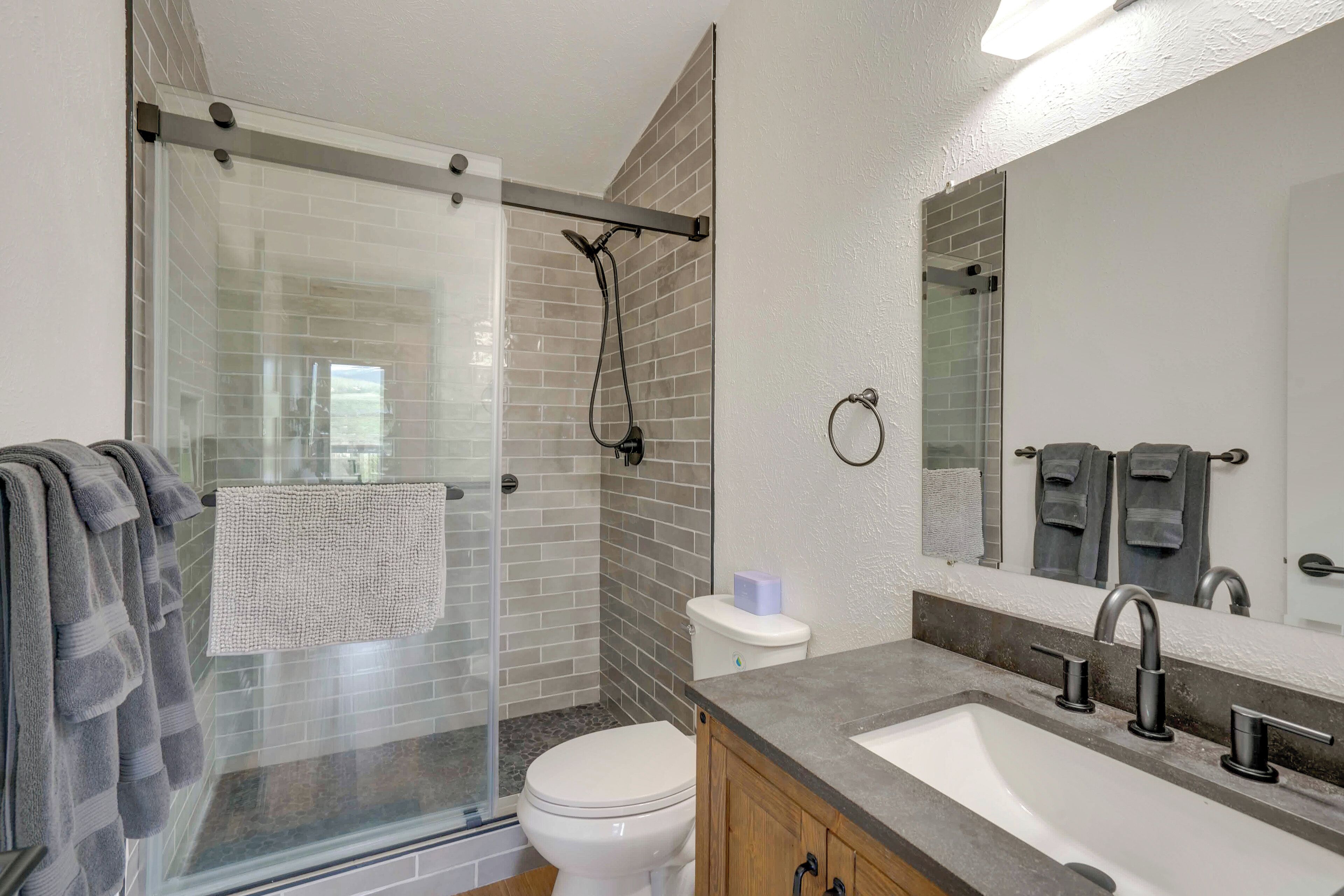 A modern bathroom with a glass shower enclosure, a white toilet, a sink with a vanity, and a large mirror.